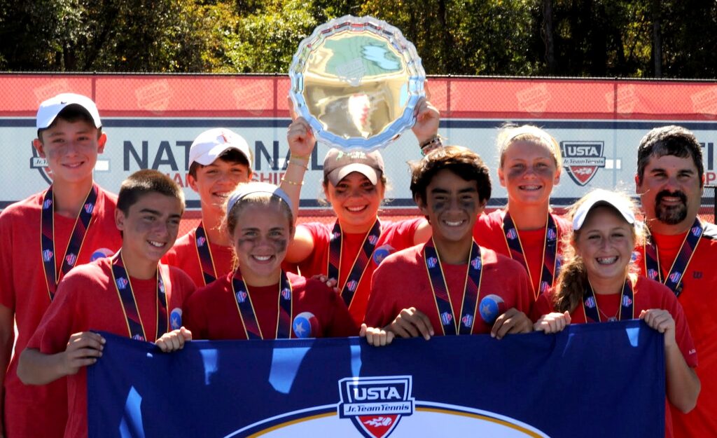 Eight smiling teens and one adult hold medals and a silver trophy tray at a USTA tennis event.