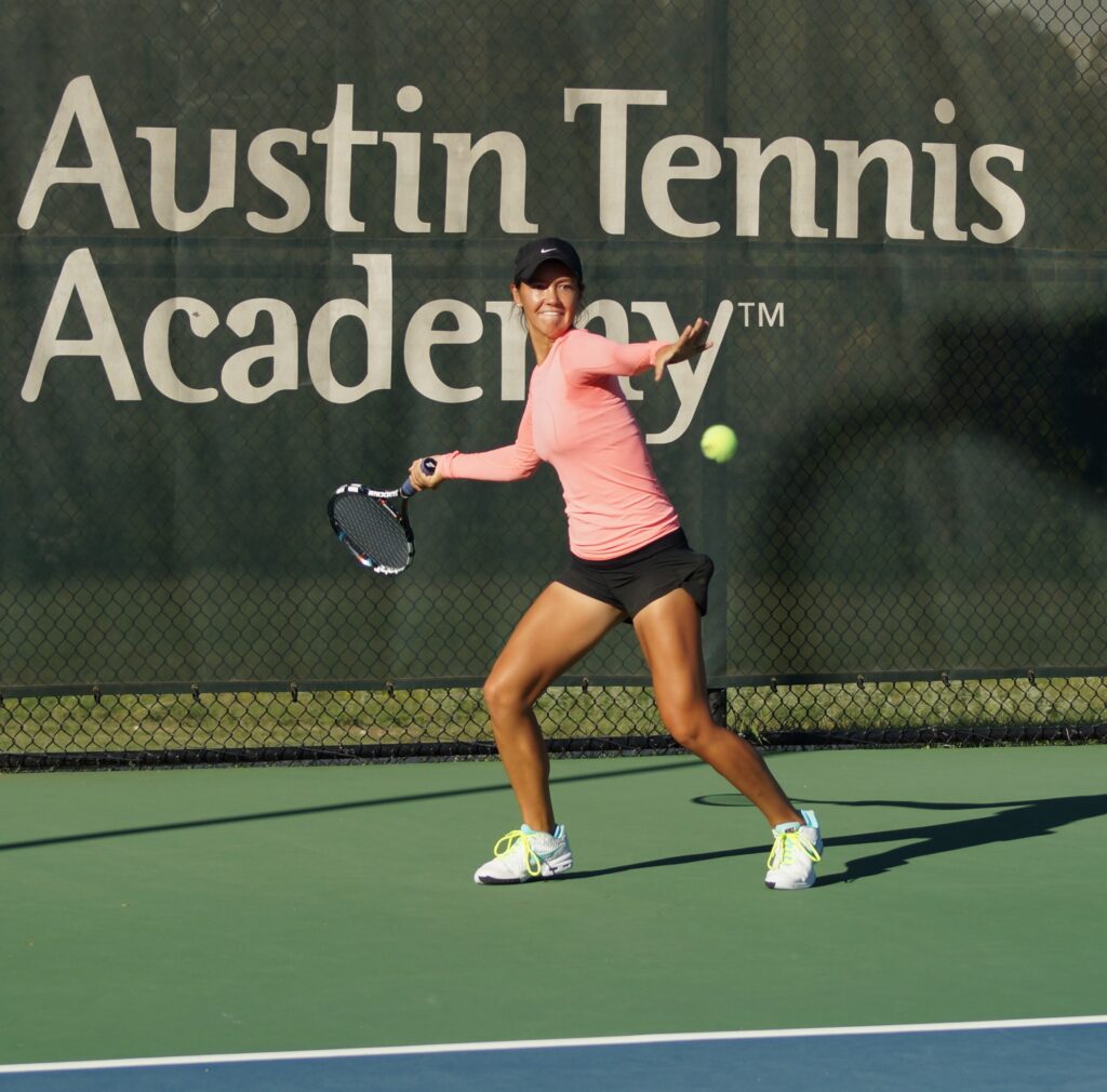 A woman in sportswear hits a tennis ball on an outdoor court at Austin Tennis Academy.