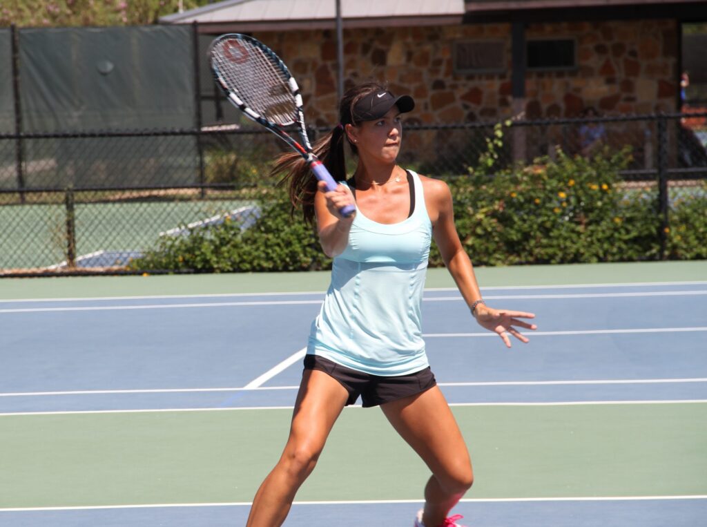 Woman in athletic wear playing tennis, preparing to hit a forehand shot on an outdoor court.