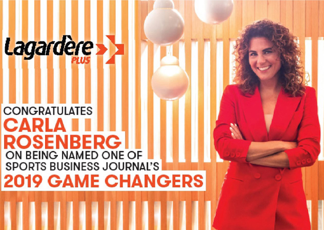 Woman in red blazer stands smiling beside a sign congratulating Carla Rosenberg as a 2019 Sports Game Changer.