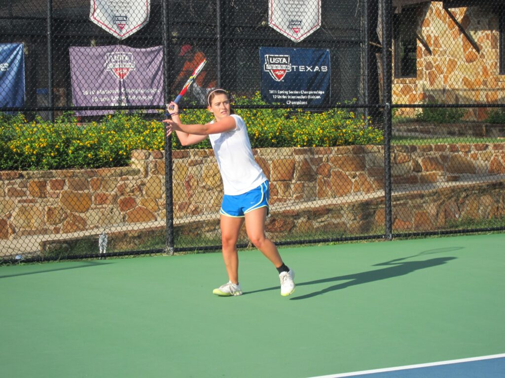 Woman in athletic wear prepares to hit a tennis ball on an outdoor court with a stone wall in the background.