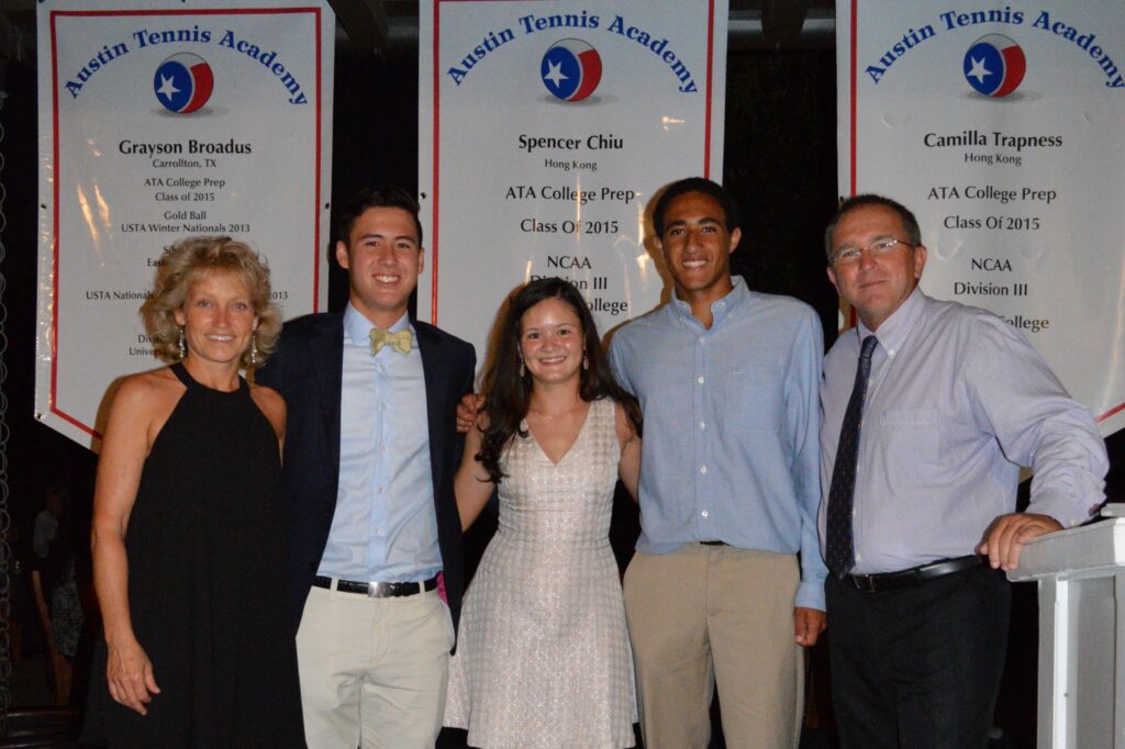 Five people stand smiling in front of banners at an Austin Tennis Academy event.