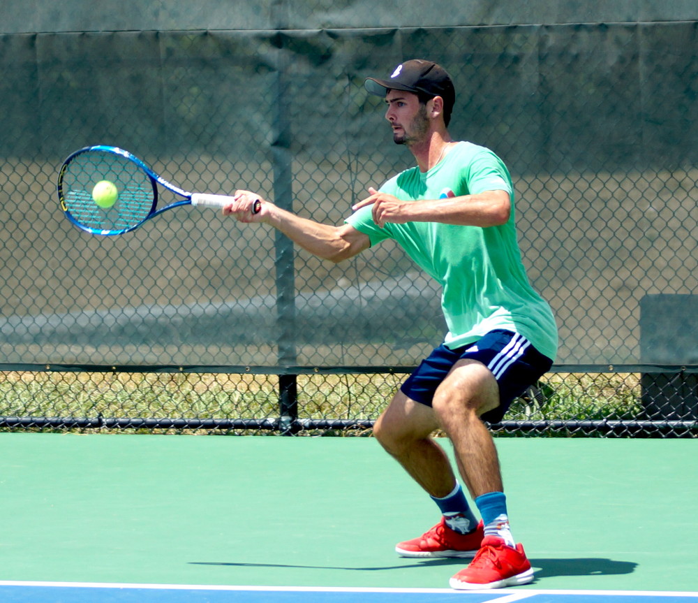A tennis player in a green shirt prepares to hit a ball with a racket on an outdoor court.