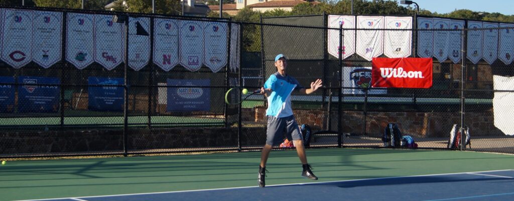 A tennis player in blue prepares to hit a forehand shot on an outdoor court with banners in the background.