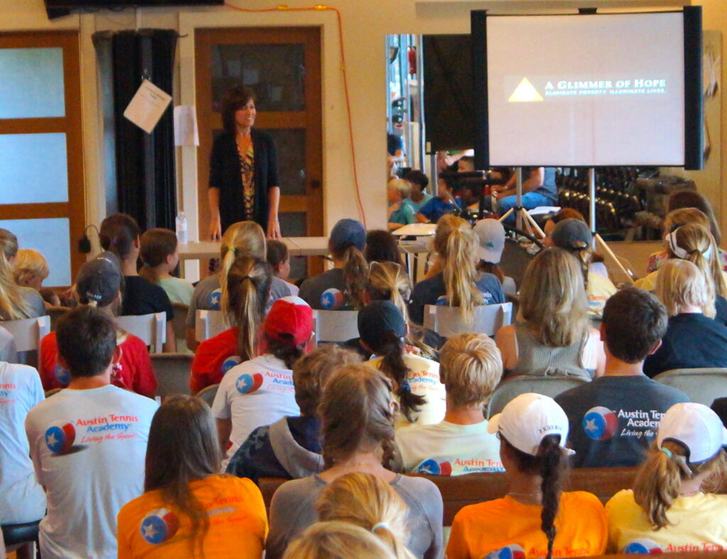 A woman speaks to a seated group of people watching a presentation titled A Glimmer of Hope.