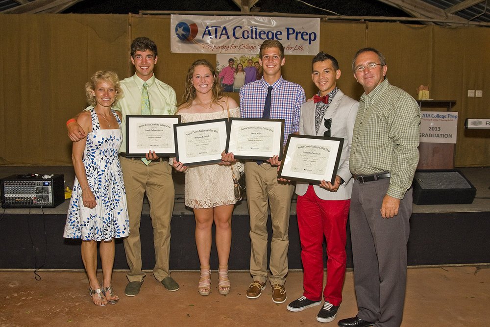Four students holding certificates stand with two adults at a graduation event, smiling for a group photo.