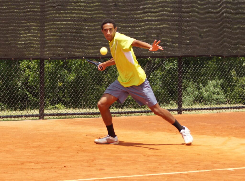 A tennis player in a yellow shirt prepares to hit a forehand shot on a clay court.