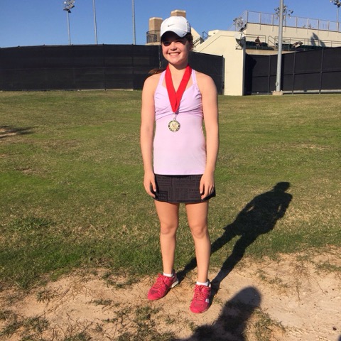 Girl in athletic clothes and a medal stands smiling on a grassy field, wearing a cap and sunglasses.