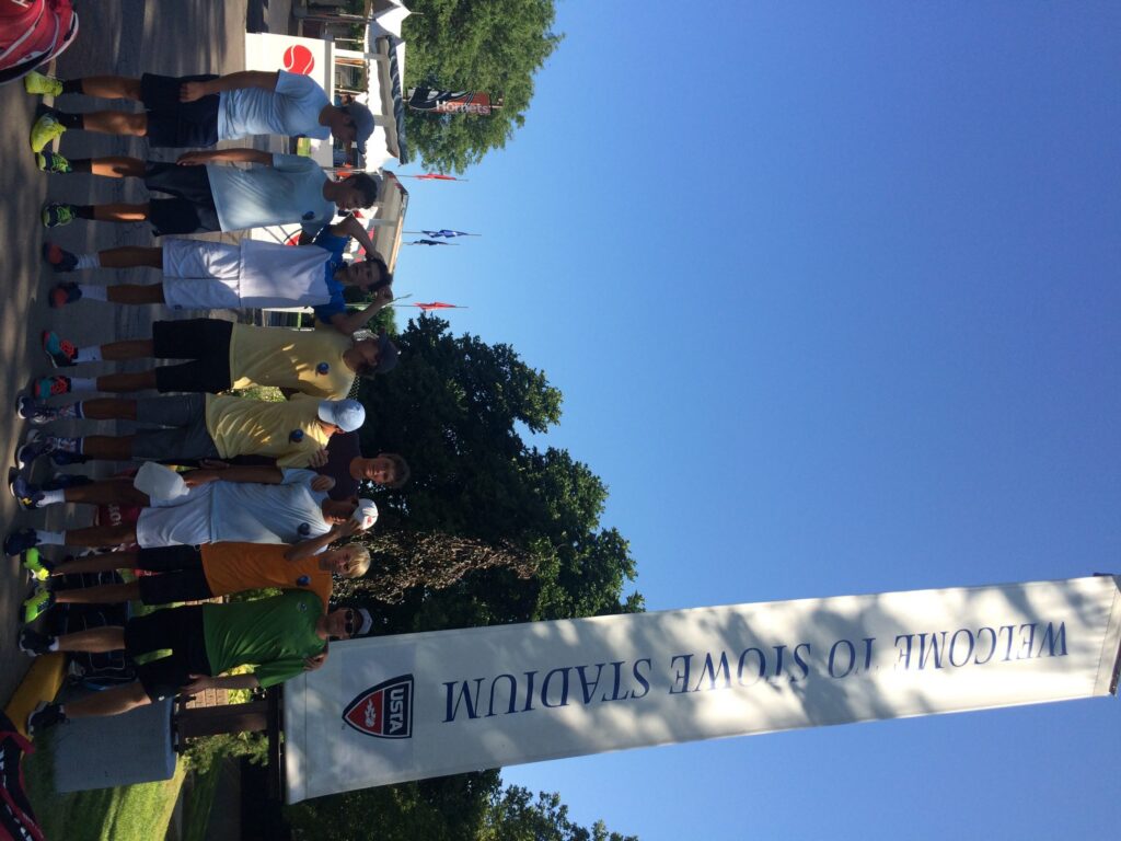 A group of people stand near a Welcome to Stowe Stadium sign on a sunny day.