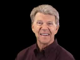 Smiling older man with gray hair wearing a dark shirt, posed against a plain black background.