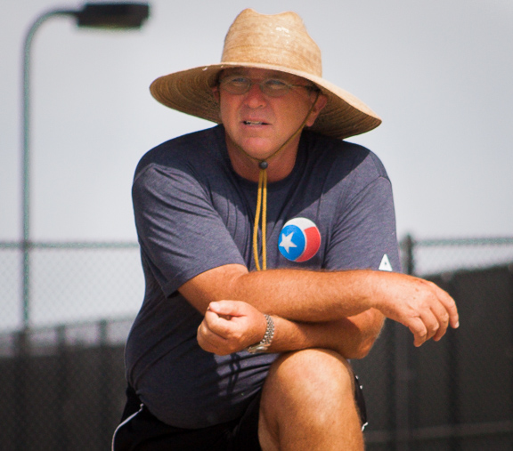 Man wearing a large straw hat and glasses, sitting outdoors near a fence, with a Texas-themed shirt.