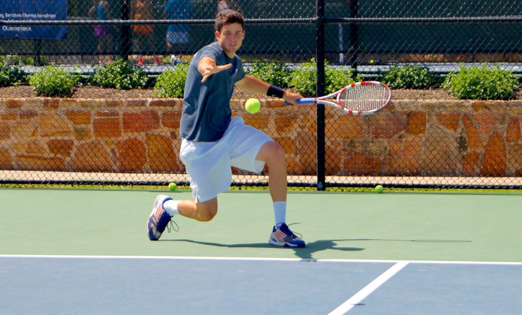 A man in sportswear lunges to hit a tennis ball with a racket on an outdoor court.