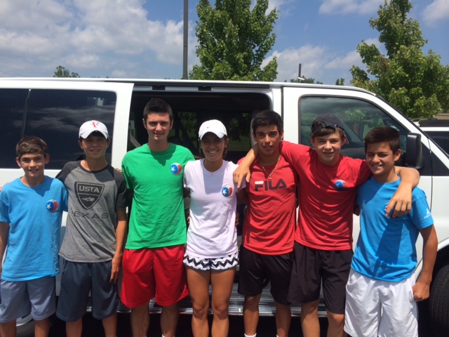 Seven teens in athletic gear stand together smiling in front of a white van on a sunny day.