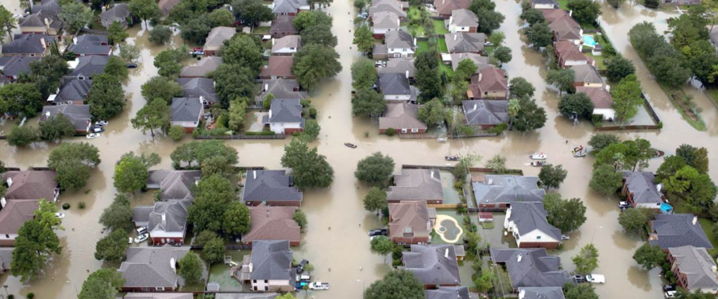 Aerial view of a flooded suburban neighborhood with streets and yards submerged in water.