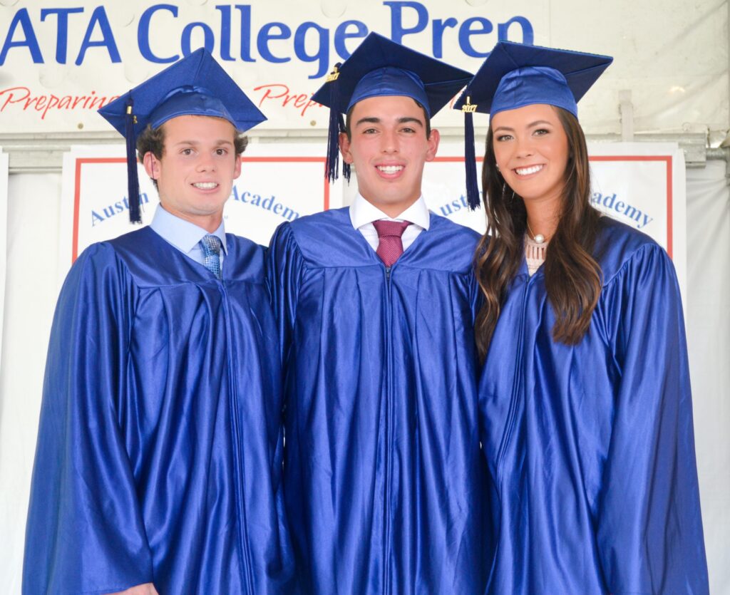 Three graduates in blue caps and gowns smile and pose together at a graduation ceremony.