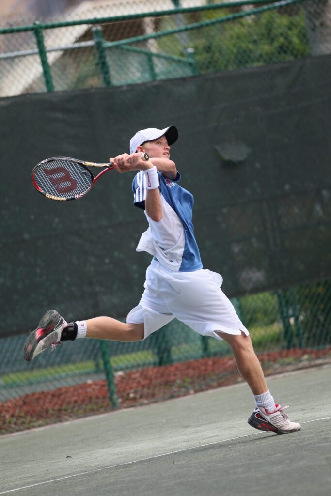 A tennis player in mid-air hitting a backhand shot on an outdoor court.